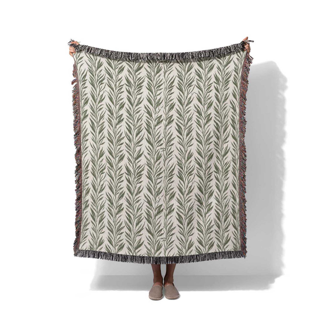 Boho woven blanket with green leaf pattern draped over a person, white background, Cuddlezzz