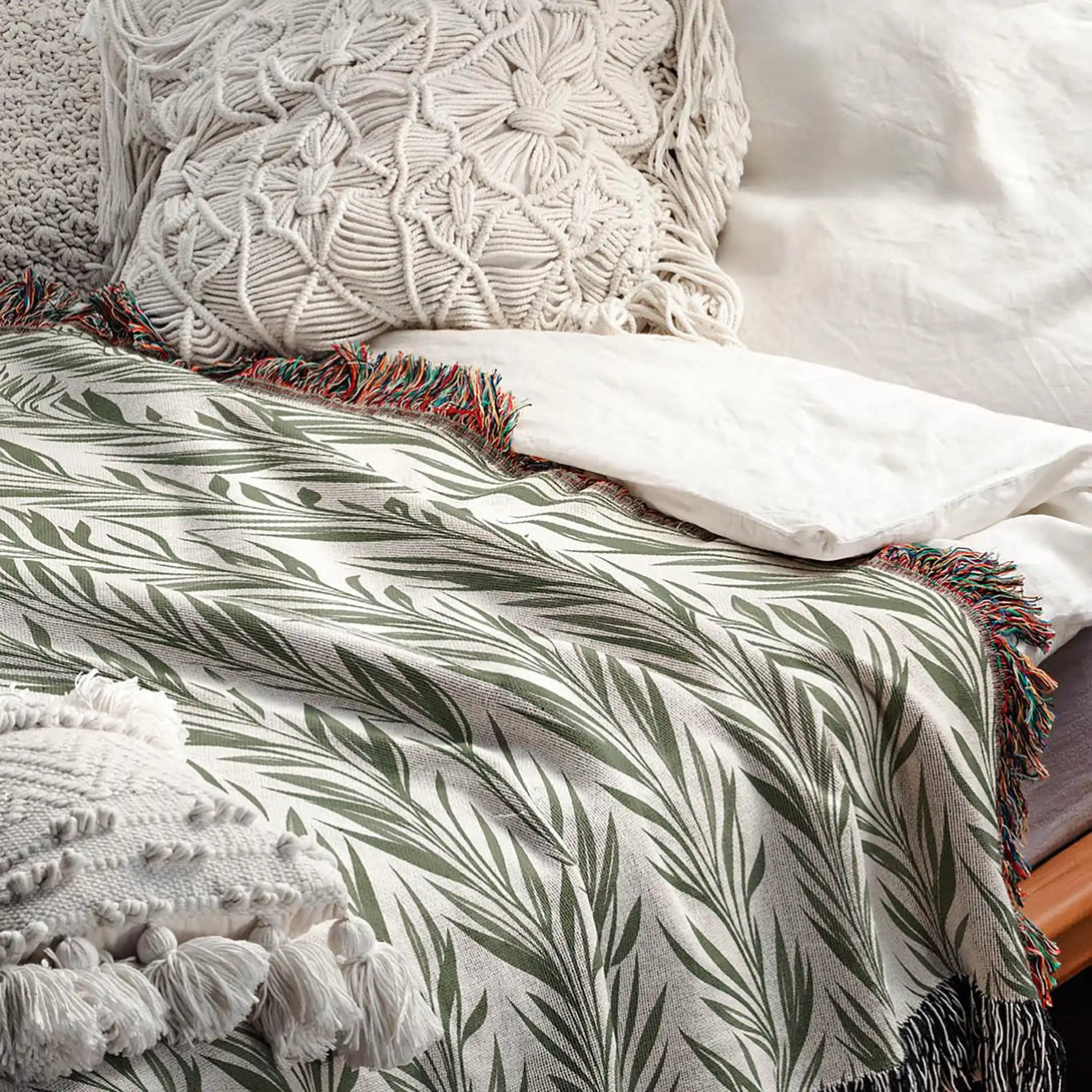 Woven cotton throw blanket with green leaf pattern on bed, styled with white boho pillows, Cuddlezzz