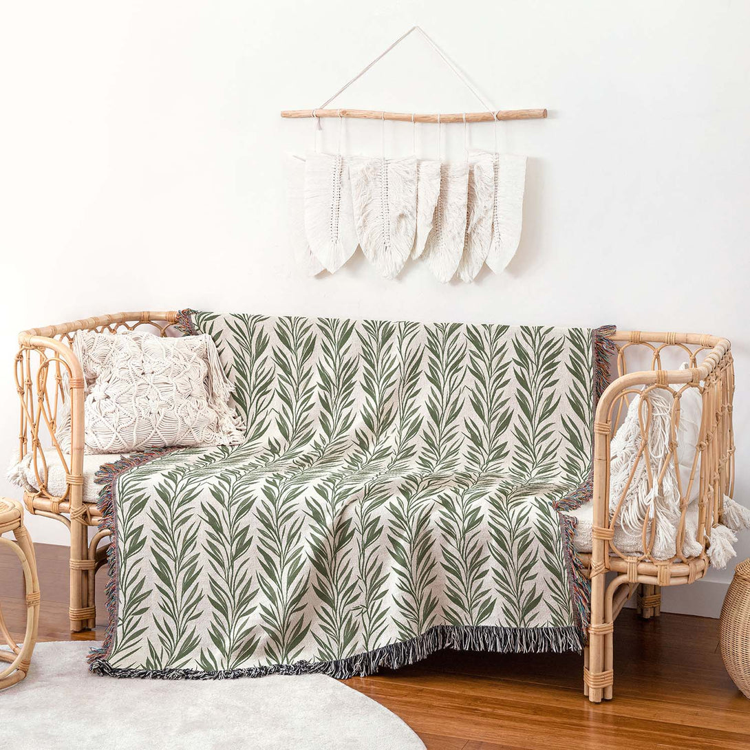 Green leaf-patterned woven throw blanket draped over a wicker chair in a cozy boho living room.