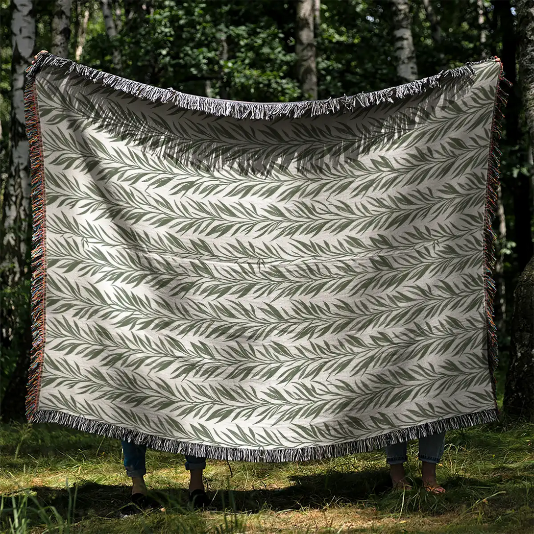 Two people holding an 80x60 woven throw blanket with a green leaf pattern in a sunlit forest.